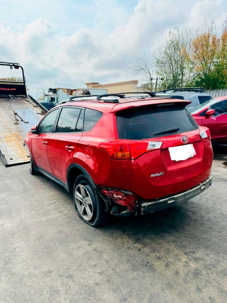 Red Toyota RAV4 with rear damage in Houston, ready for towing pickup.