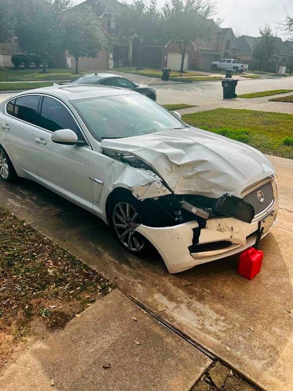 Wrecked white jaguar parked in driveway, bought as-is by Zeus Cash For Junk Cars Houston.