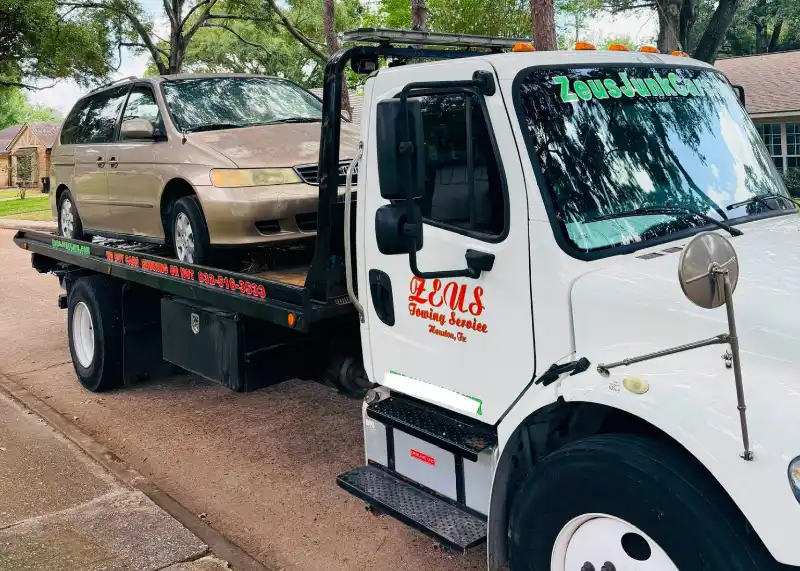 Beige Honda Odyssey loaded on a Zeus Cash For Junk Cars tow truck in a residential area.