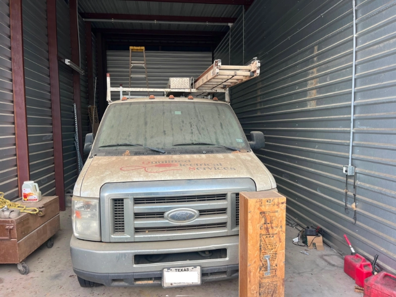 Dusty Ford work van with roof ladder parked inside a storage unit.