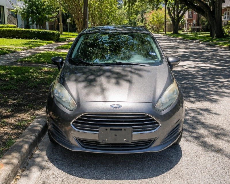 Front view of a gray Ford Fiesta parked on a tree-lined residential street in Pasadena, TX.