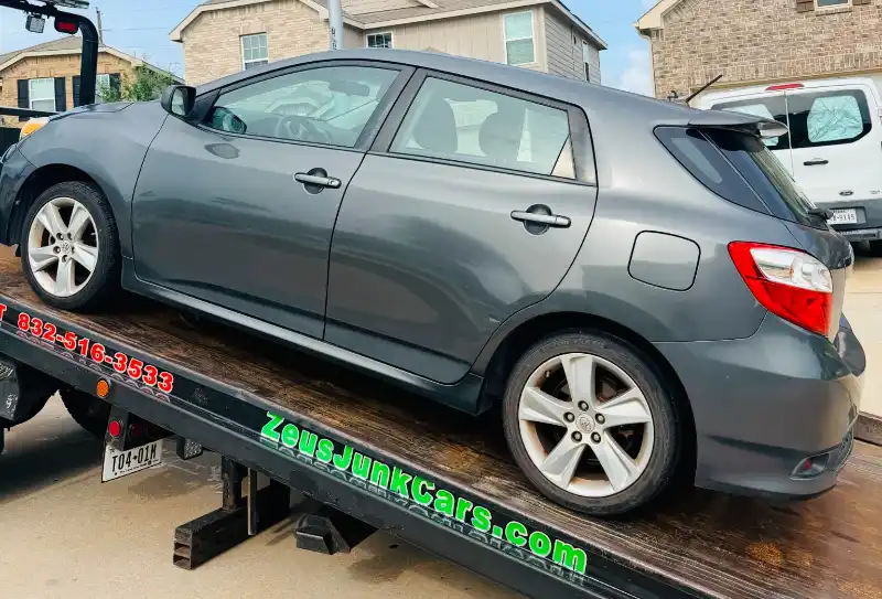 Gray Toyota Matrix loaded on a Zeus Cash For Junk Cars tow truck in Houston, TX.