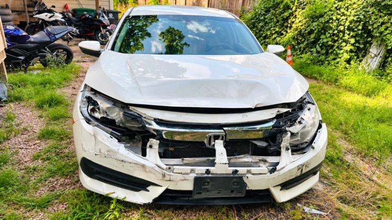White Honda Civic with severe front-end damage parked beside motorcycles on gravel.
