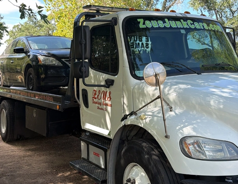 White Zeus Cash For Junk Cars tow truck hauling a black sedan in Cypress, TX.