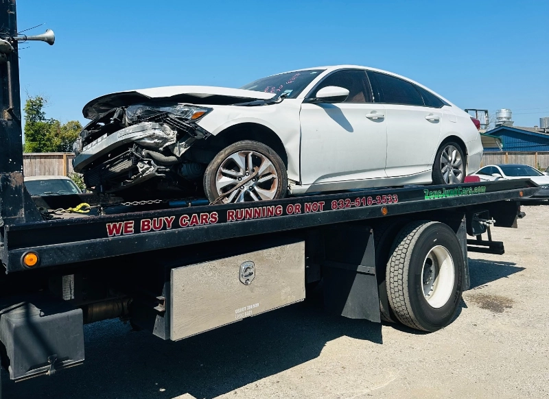Damaged white sedan loaded on Zeus tow truck in the Houston area.